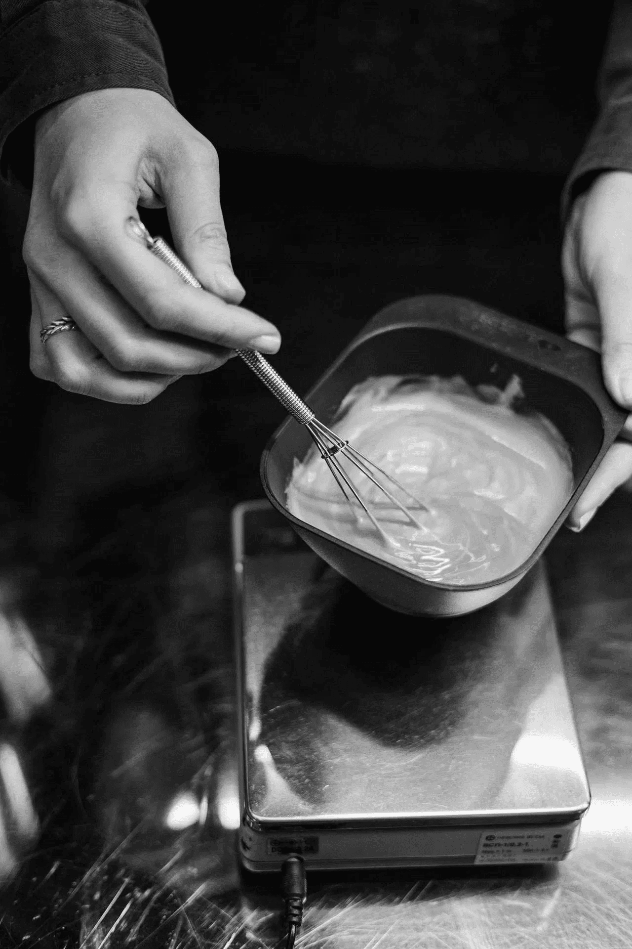 Mixing hair dye with whisk in a small black bowl on digital scale.