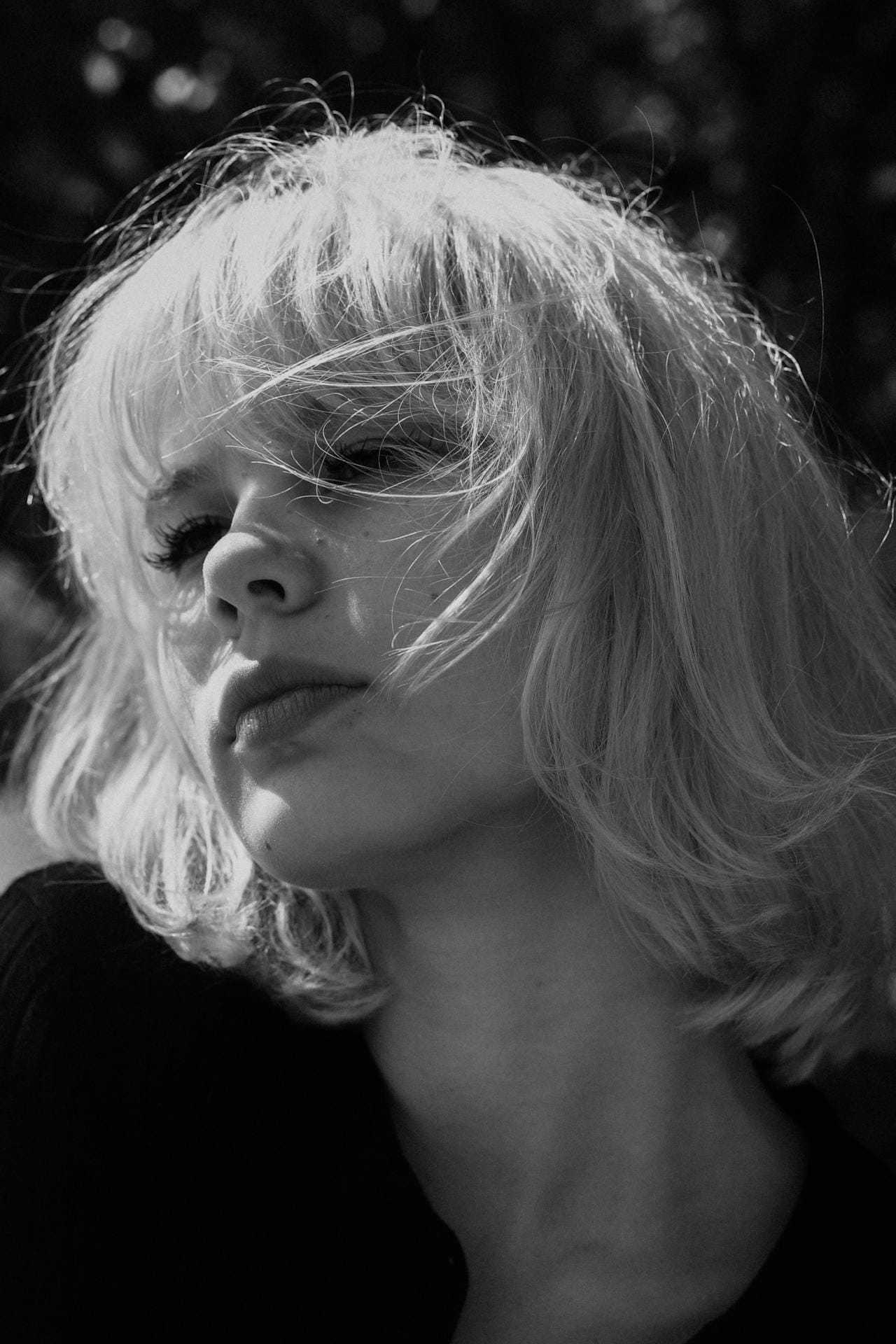 Young woman with short, wind-swept hair, gazing upwards in black and white.