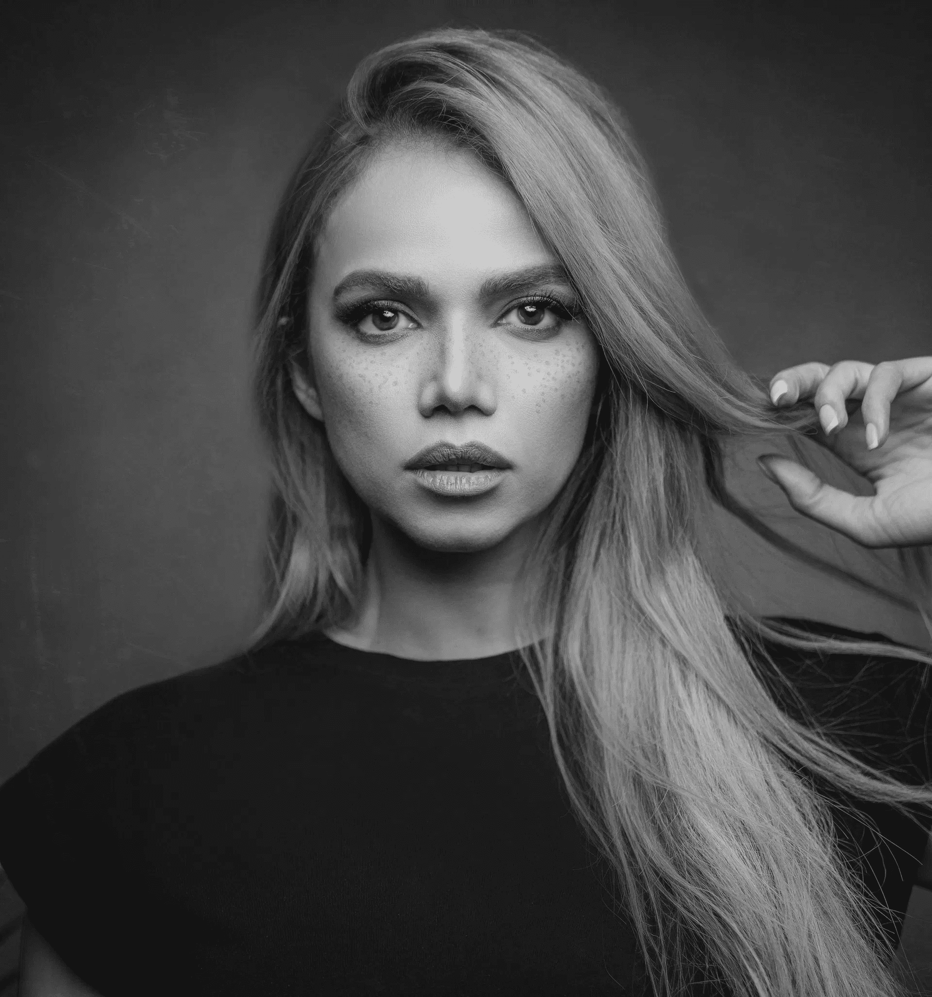 Red-haired woman with striking makeup, wearing a black top against a dark background.