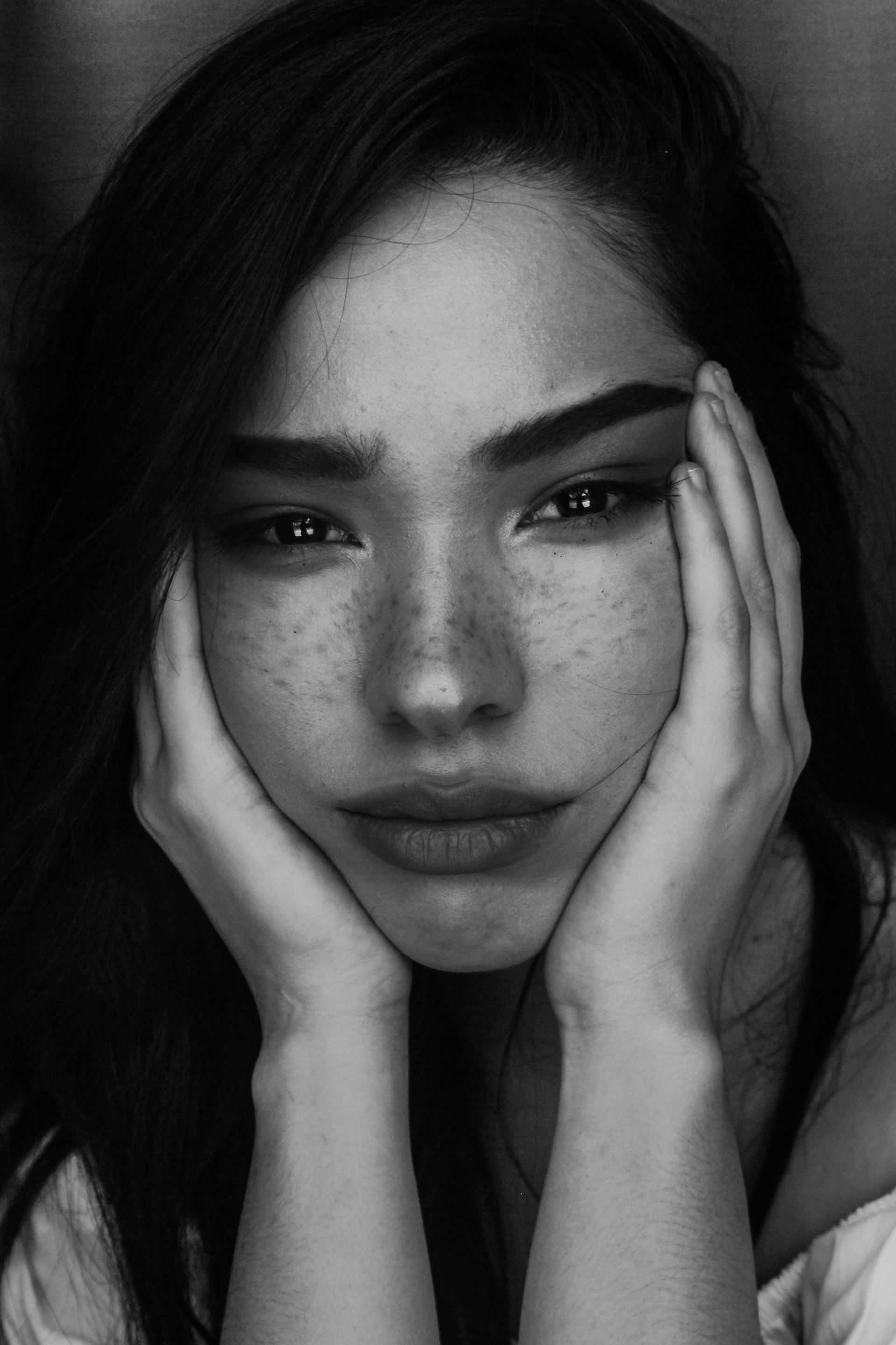 Young woman with freckles, resting her face in her hands, looking directly at the camera.