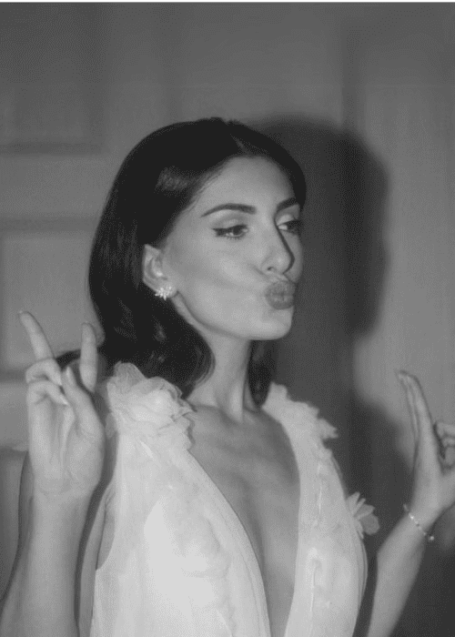 Woman in a white dress making a duck face and peace signs with both hands.